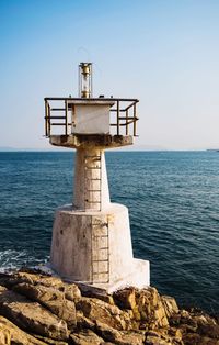 Lighthouse on rocky shore against sky on sunny day