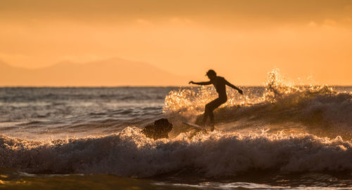 Silhouette man surfing in sea against sky during sunset