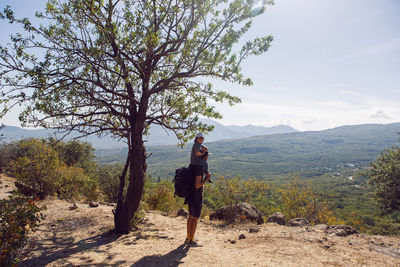 Father with a backpack and his son stands next to a tree on a mountain in the summer in the crimea