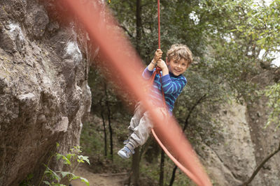 A four year old toddler plays and swings hanging from a climbing rope
