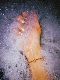 Cropped hand of woman amidst soap sud in bathtub