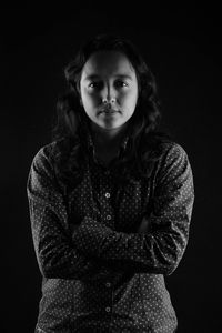 Portrait of woman with arms crossed standing against black background