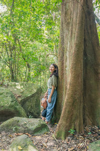 Portrait of happy young woman standing by tree trunk in forest