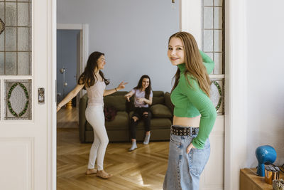 Portrait of smiling young woman standing at doorway near friends dancing in living room