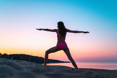 Full length of woman with arms raised against sky during sunset