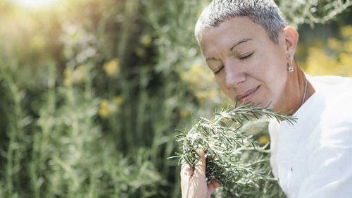 Woman with eyes closed smelling while holding rosemary