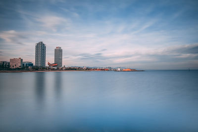 Sea by modern buildings against sky in city