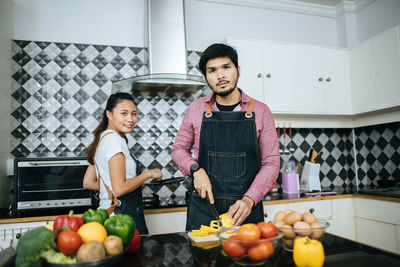 Portrait of young man and woman cutting vegetables in kitchen