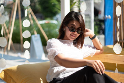 Full length of woman sitting wearing sunglasses while sitting outdoors