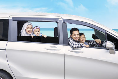 Portrait of smiling family looking through window while sitting in car