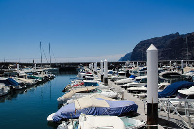 Boats moored at harbor against clear blue sky