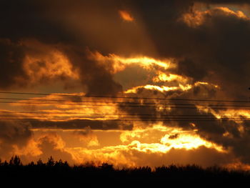 Silhouette trees against dramatic sky during sunset