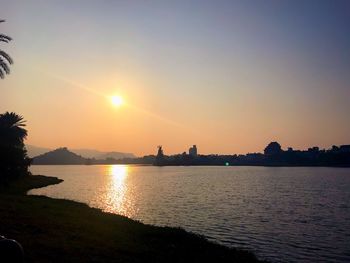 Scenic view of river by silhouette buildings against sky during sunset