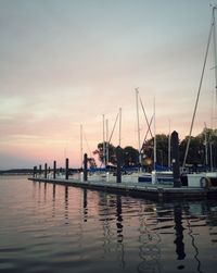 Sailboats moored at harbor against sky during sunset