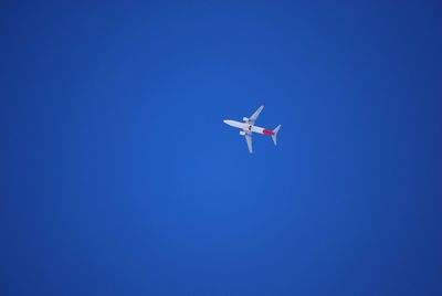 Low angle view of airplane flying against clear blue sky