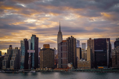 Aerial view of buildings by river against cloudy sky during sunset