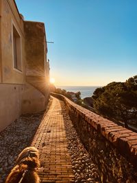 Footpath amidst sea against clear sky during sunset