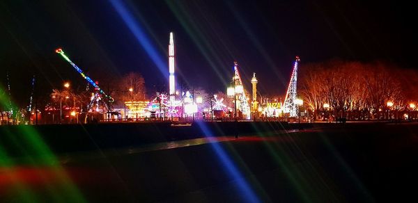 Illuminated city by river against sky at night