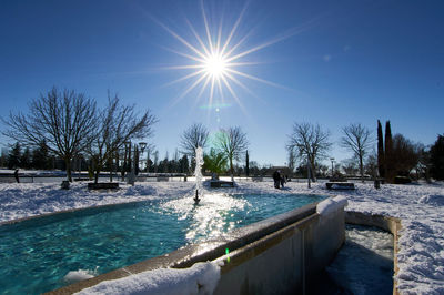 Horizontal close-up of water fountain in park surrounded by snow with blue sky and sunshine