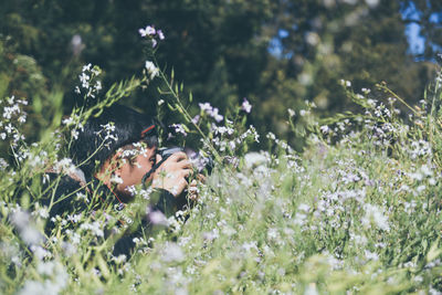 Side view of mid adult man photographing amidst flowers in forest