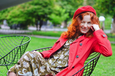 Young happy woman with red hair, freckles, beret, coat walking in autumn park, drinking coffee