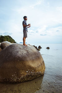 Side view of man standing on rock by sea against sky