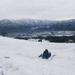 Man sitting on snow covered mountains against sky