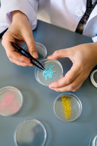 Unrecognizable female chemist technician examining a blue glitter sample over petri dish on lab