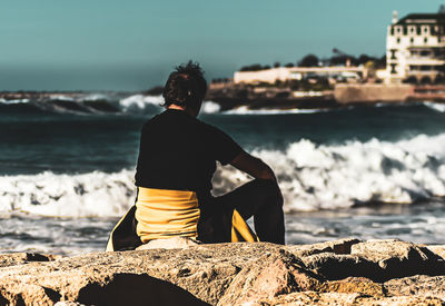 Rear view of man sitting on rock by sea