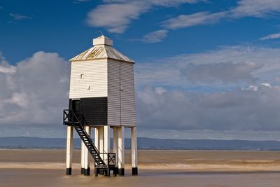 Lifeguard hut or lighthouse on beach against blue sky