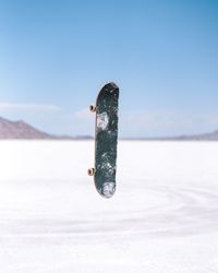 Skateboard in mid-air over snow covered field against sky
