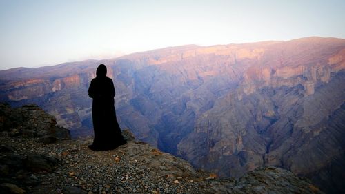 Rear view of woman standing on cliff against clear sky