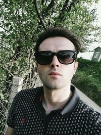 Portrait of young man wearing sunglasses against trees