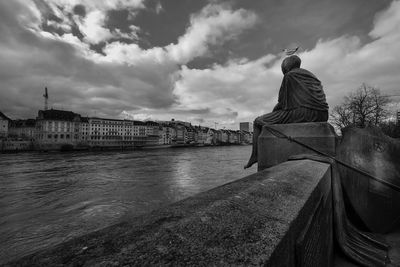 Rear view of person by river against buildings