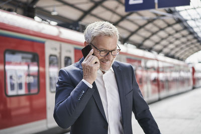 Smiling male professional talking on mobile phone at railroad station