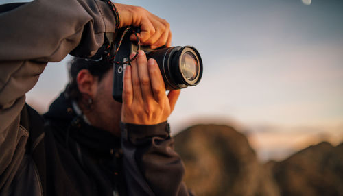 Side view of unrecognizable male photographer with professional photo camera taking pictures of nature while standing on top of rocky mountain