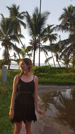 Young woman standing at beach against trees