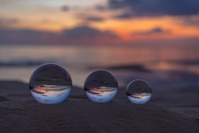 Close-up of glasses on beach against sky during sunset