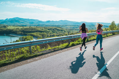 Rear view of women walking on road against mountain