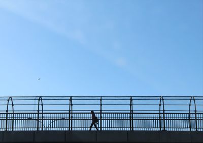 Rear view of silhouette woman walking on railing against sky
