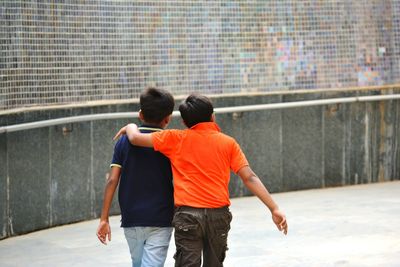 Rear view of male friends walking on footpath by wall