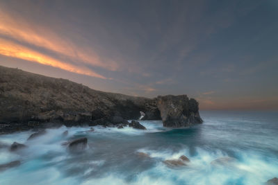 Scenic view of sea by rock formation against sky during sunset