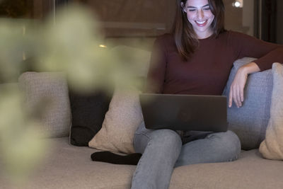 Young woman using laptop while sitting on sofa at home