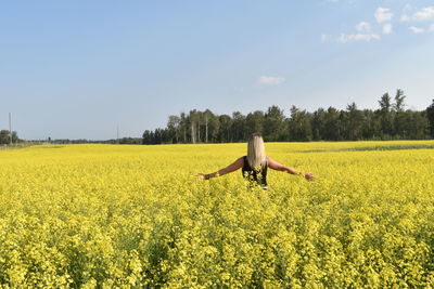 Woman with arms outstretched standing amidst yellow flowering plants