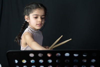 Girl playing drum while standing against curtain