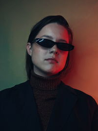 Portrait of young woman wearing sunglasses against wall