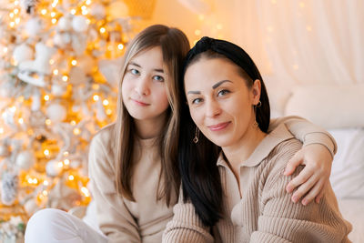 Happy mom and daughter cuddle on bed in decorated bedroom on christmas eve