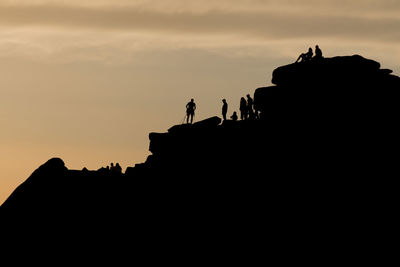 Silhouette of lots of people watching a climber at the summit of stanage edge. 