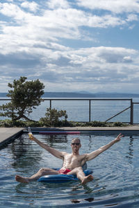Full length of shirtless man holding beer bottle on pool raft at swimming pool