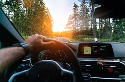 Cropped hand of man driving car during sunset